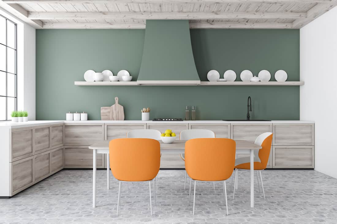 Green kitchen with L-shaped countertop, table and orange chairs