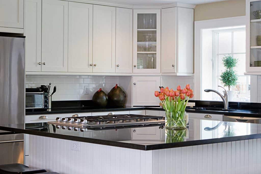 Home interior kitchen painted in white, brightly lit, with a good view of black granite countertop