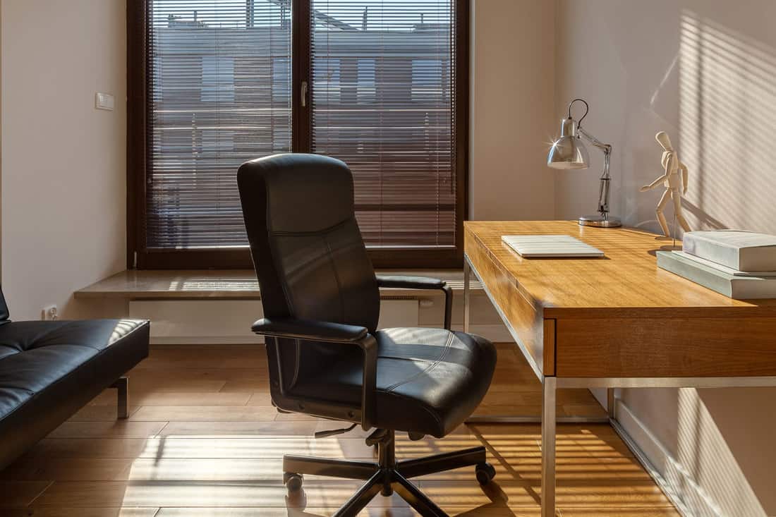 Home office with big window, wooden desk and floor and black office chair and sofa, How to Fix an Office Chair That Leans Back