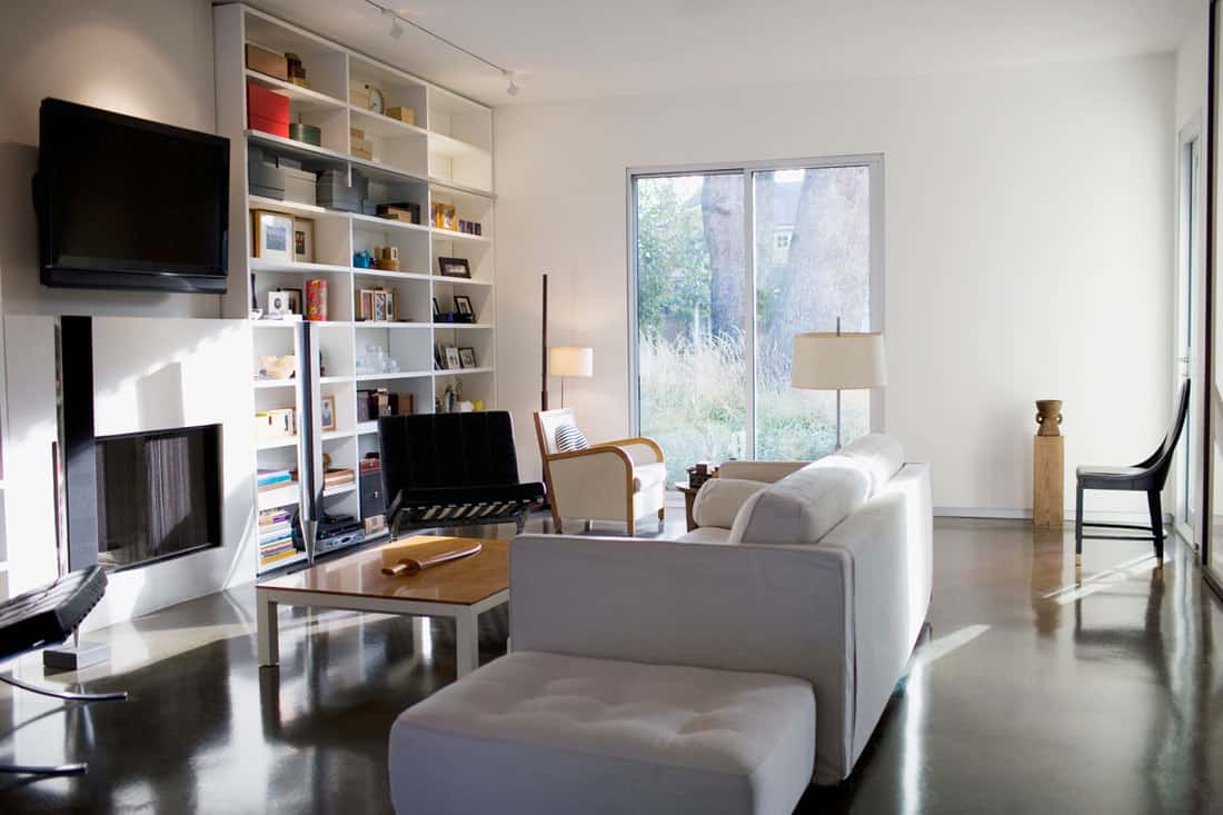 Interior of a contemporary designed living room with walls painted in white, a tall bookshelf, and a white sofa in the center