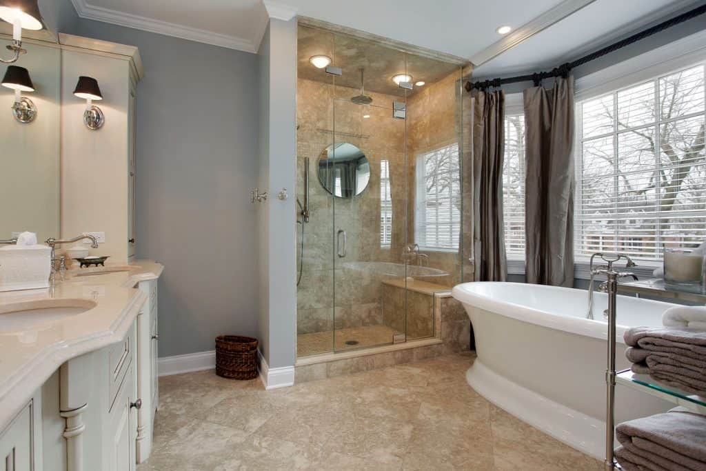 Intérieur d'une luxueuse salle de bains moderne avec une douche en faux carrelage, une baignoire blanche près de la fenêtre et un meuble-lavabo en bois