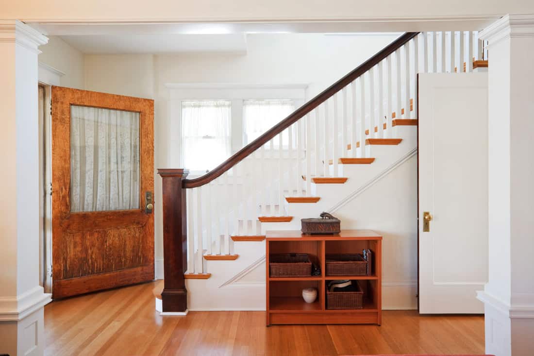interior of a modern contemporary foyer section with white painted walls, wooden steps, and a hardwood door with a glass window, How Tall Should Lamp Be On Foyer Table?