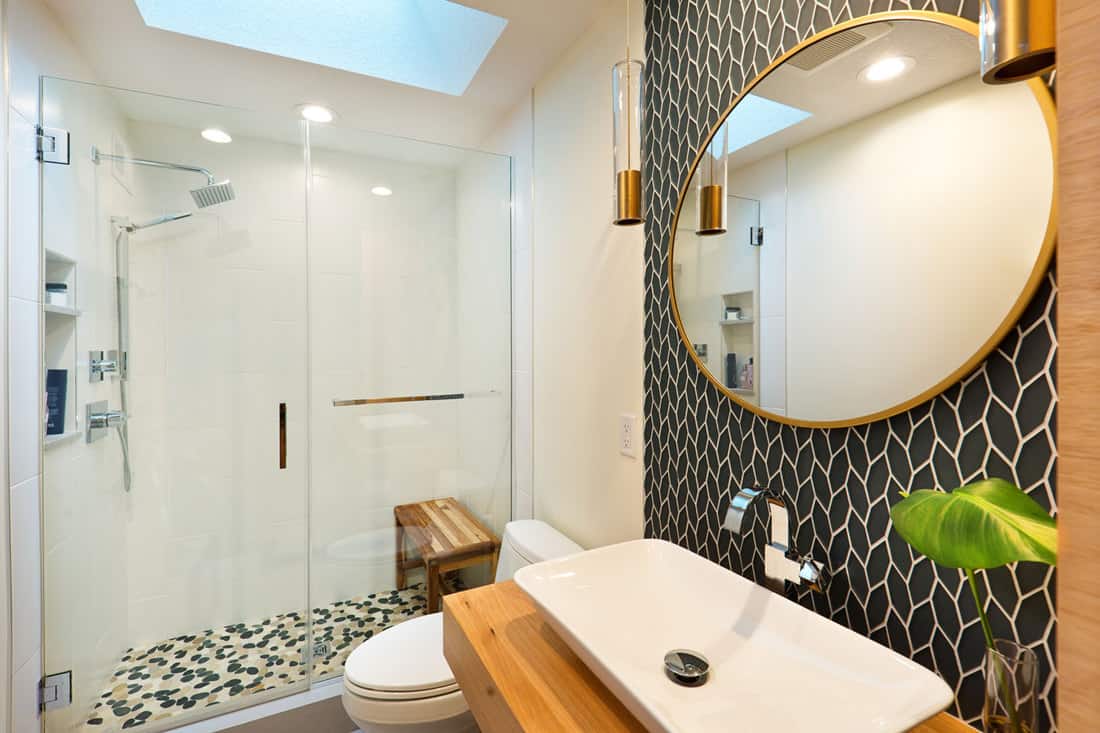 Interior of an ultra modern contemporary bathroom with a wooden vanity, huge round mirror, and a glass wall shower area with a wooden shower bench, 11 Walk-in Shower With Seat Designs