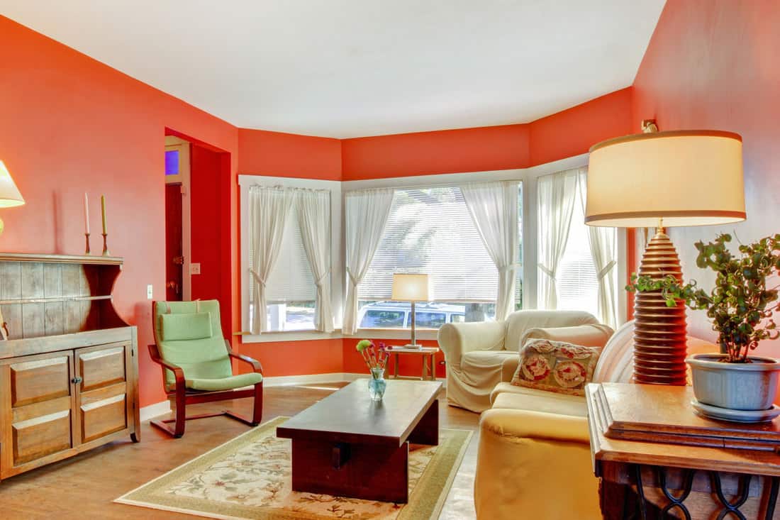Grand salon rouge avec du bois dur, des rideaux blancs et des meubles anciens, Quels rideaux vont avec des murs rouges ?