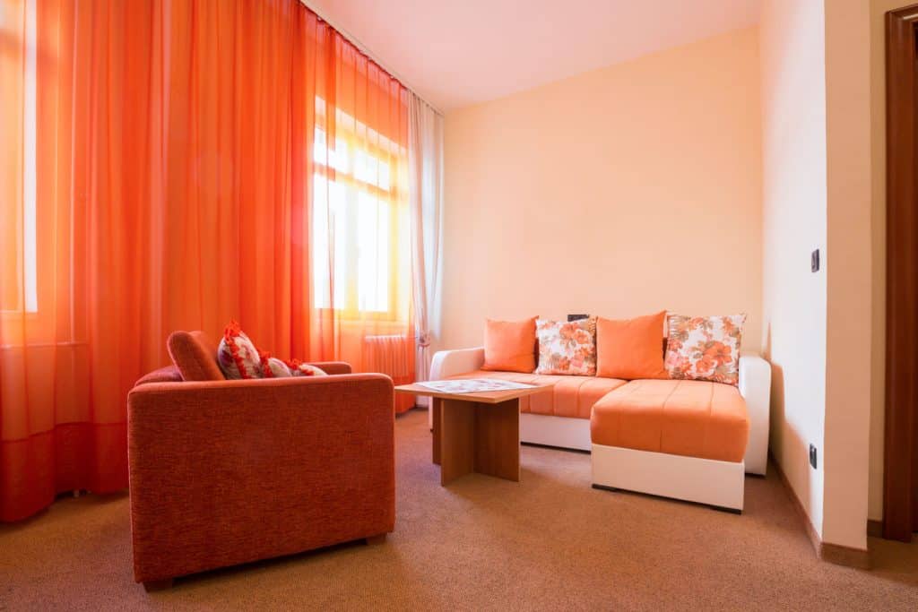 Salon avec moquette beige, canapé à bras carré et rideaux orange