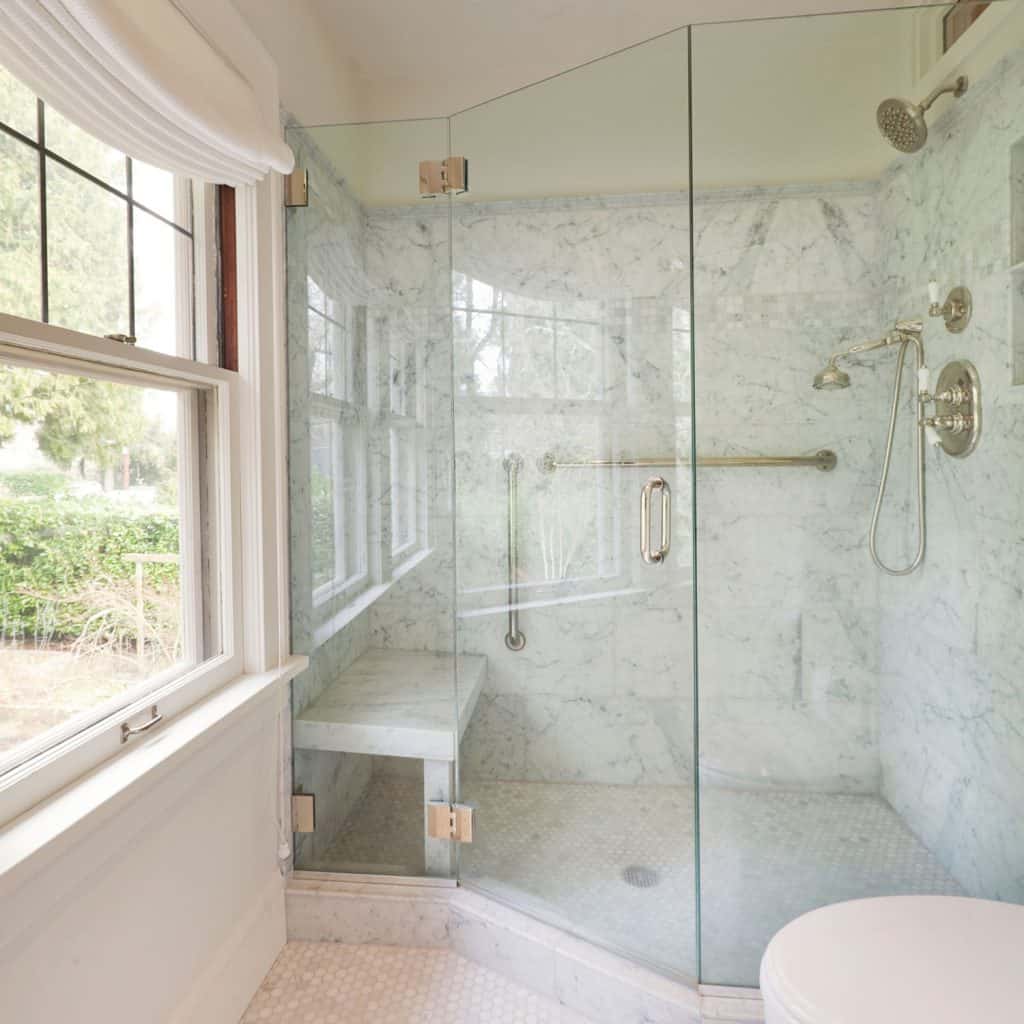 Salle de bain moderne avec une douche murale en verre, des murs en faux carrelage, une immense fenêtre et un petit banc de douche