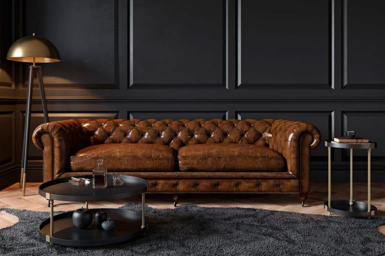 A modern classic black interior with capitone brown leather chester sofa, floor lamp, coffee table, carpet, wood floor and mouldings, What Coffee Table Goes With Brown Leather Couch