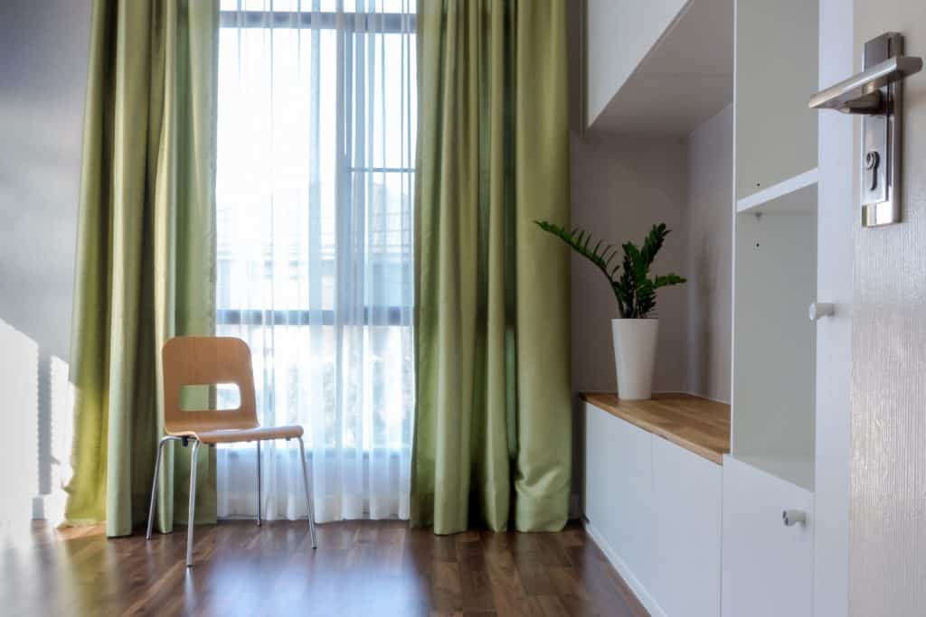 Salon contemporain moderne avec des rideaux verts, du parquet et une armoire peinte en blanc avec une plante d'intérieur