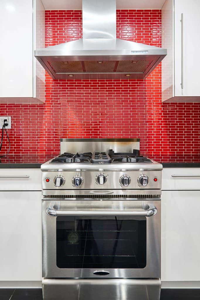 Modern designed kitchen with white cabinets, red back splash, stainless steel range oven and hood