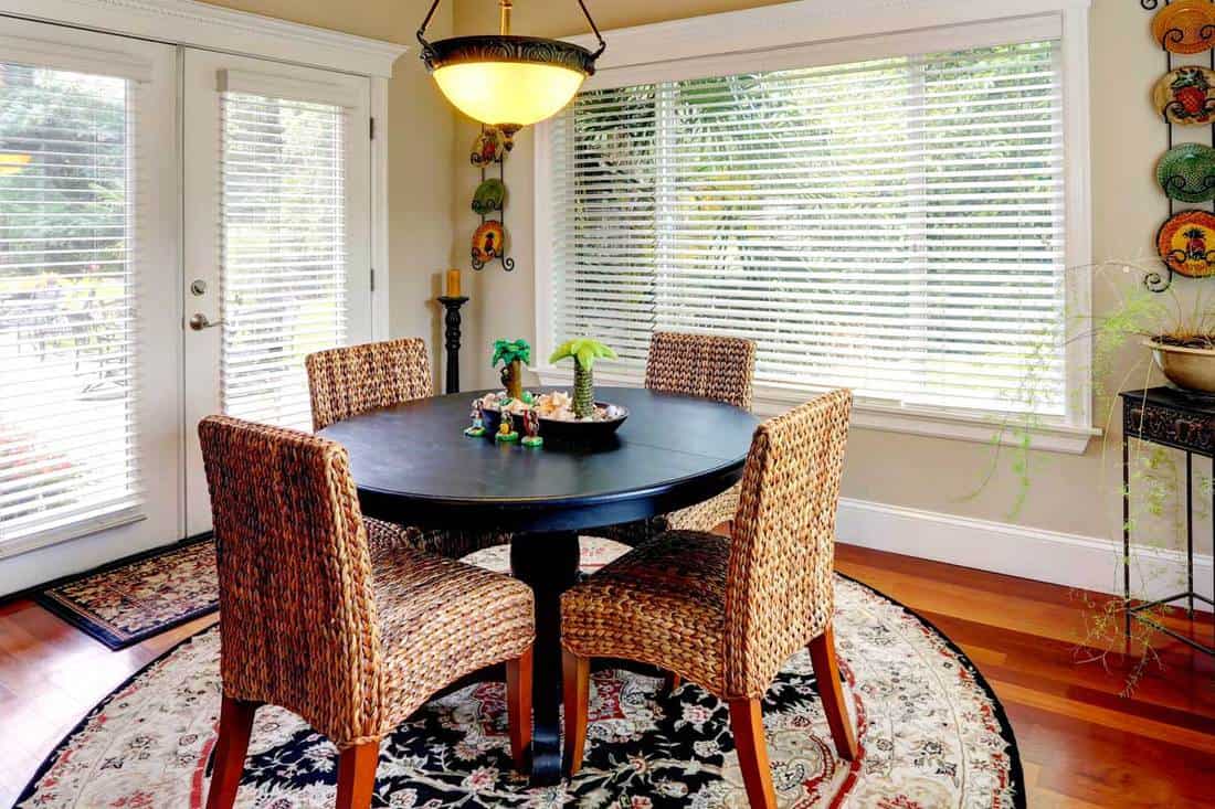 Dining room interior with round black table and wicker chairs, What Size Rug Do I Need? [A Complete Guide]