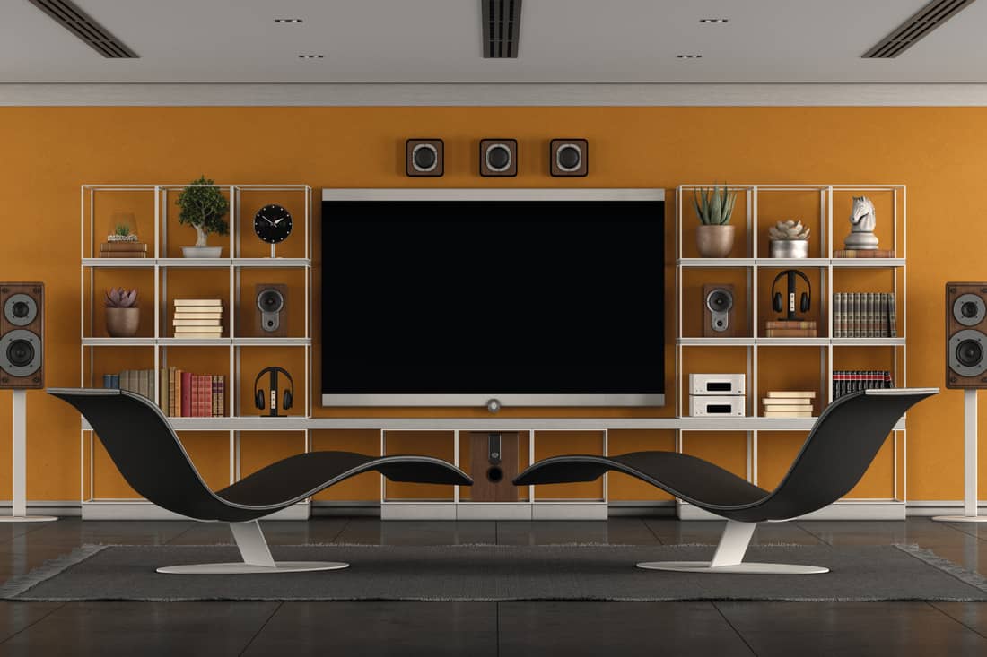 Modern living room with home cinema system with large flat screen, bookcase and two chaise lounges, modern chaise lounges and an entertainment setup