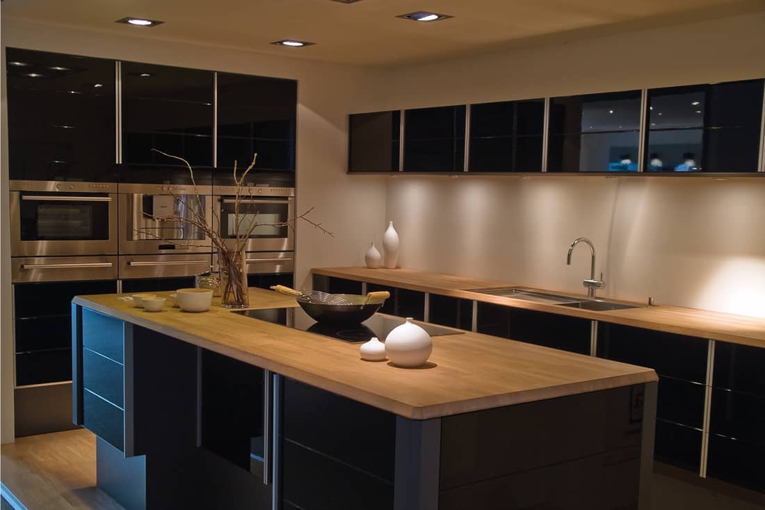 Modern trendy design black wooden kitchen, black and tan, kitchen island and large ovens on the side