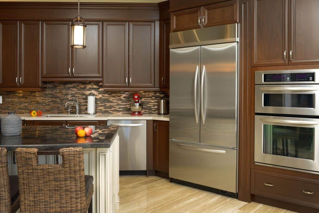 Modern vintage themed kitchen with dark wooden cabinetry with a double door fridge, dual oven, and a black granite breakfast bar