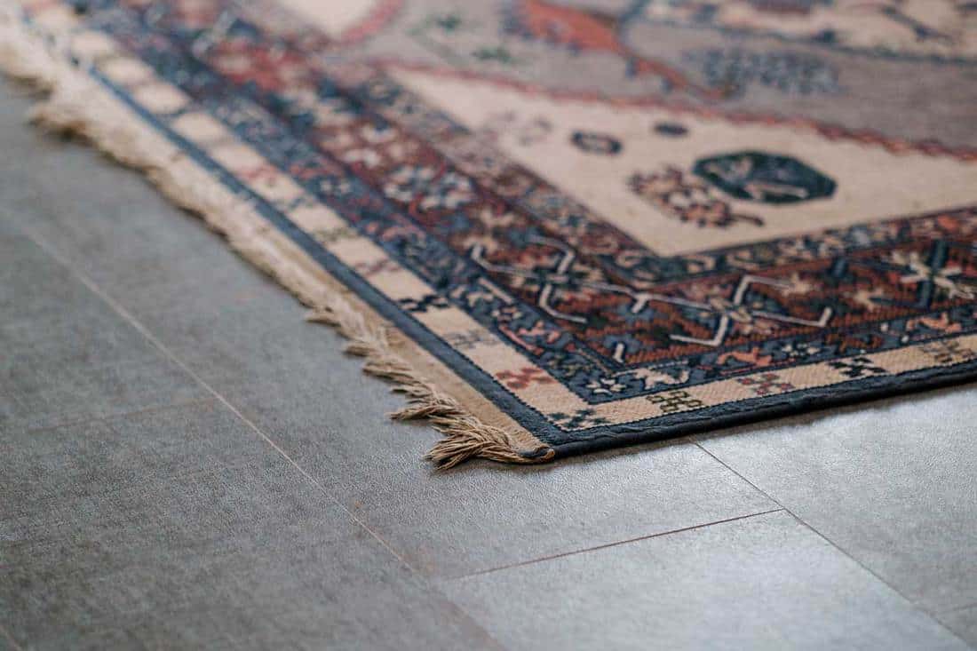 Ornamental design carpet on gray tile floor, 5 Best Area Rug Pads For Tile Floor