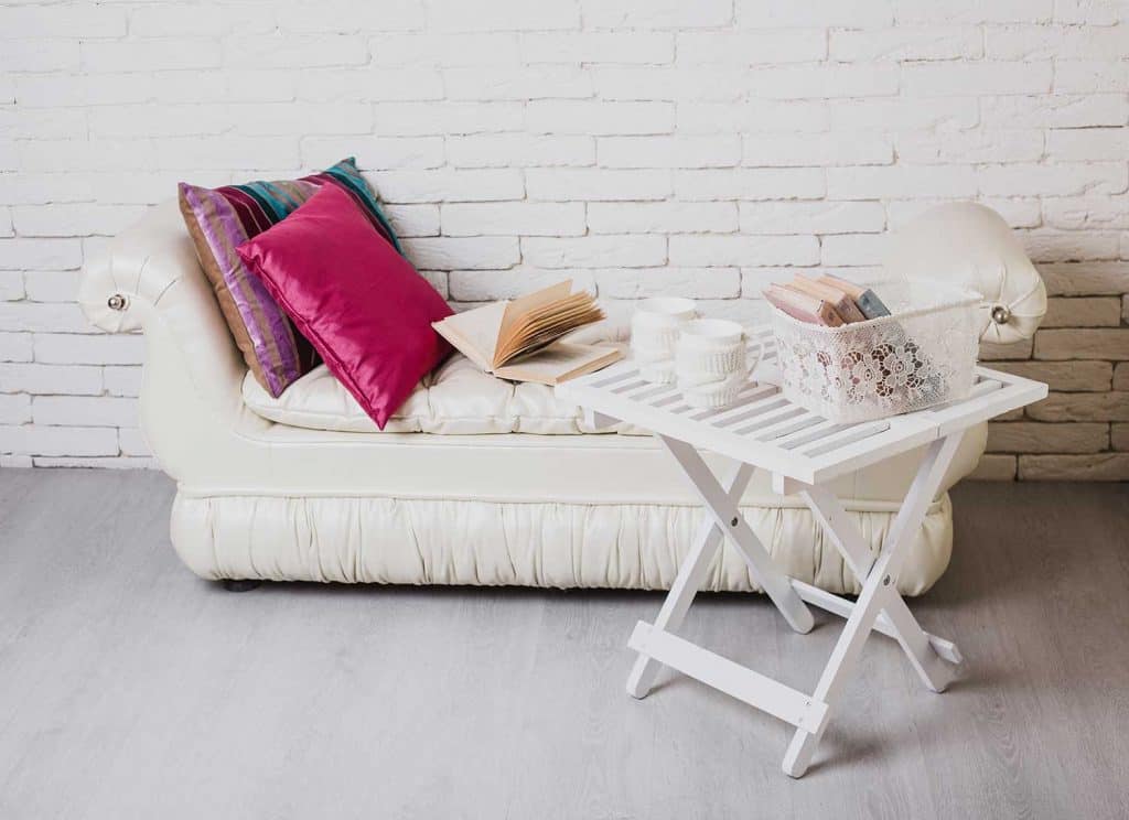 Partie de l'intérieur avec canapé et oreillers décoratifs, table en bois blanche avec des livres dessus