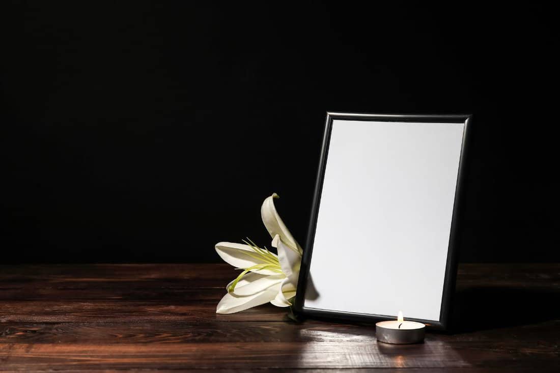 Photo frame with lily flower and candle on table against dark background