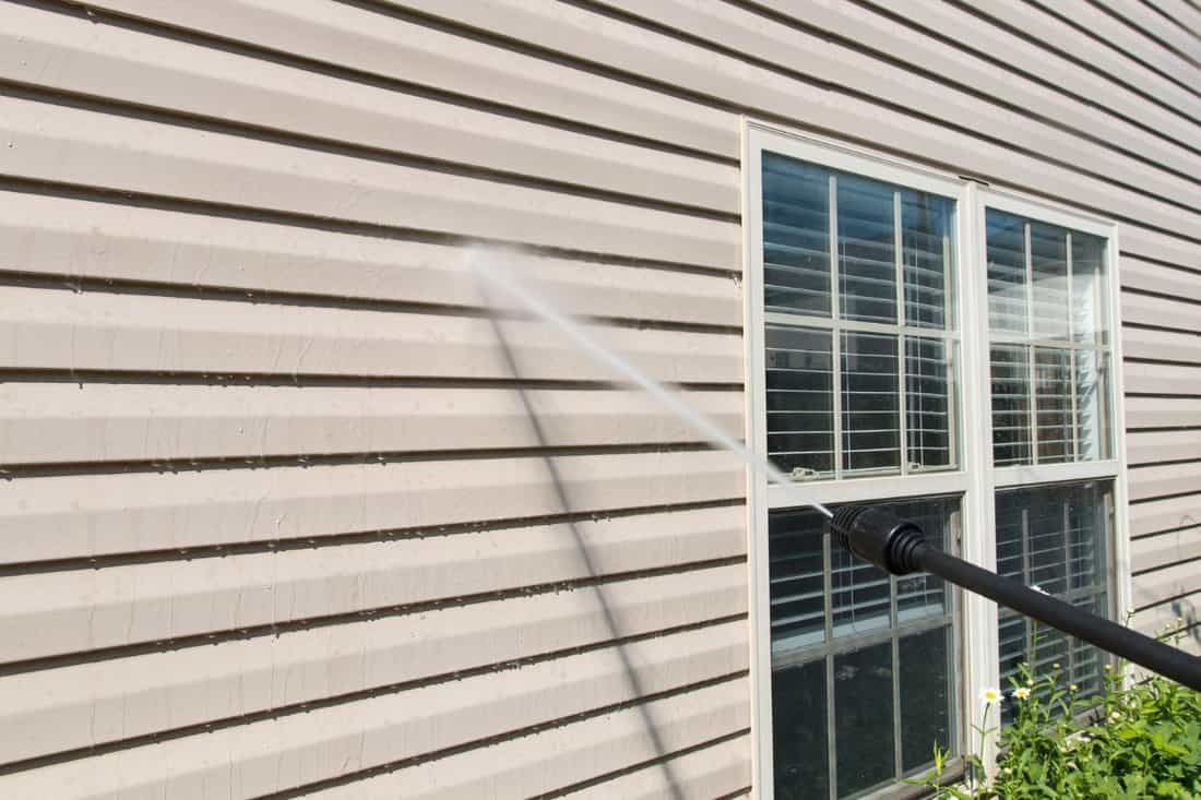 Power washing. House wall vinyl siding cleaning with high pressure water jet.
