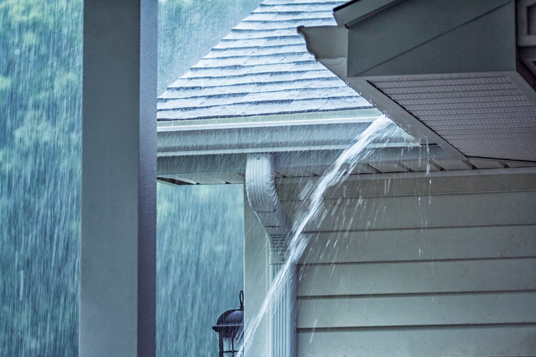 Rain storm water is gushing and splashing off the tile shingle roof and vinyl siding