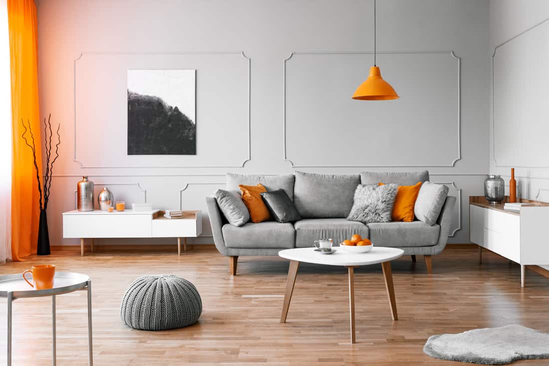 Spacious contemporary themed living room with a laminated flooring, gray sofa, with throw pillows, and a small ottoman near the coffee table, How To Decorate A Den? [4 Room Options]