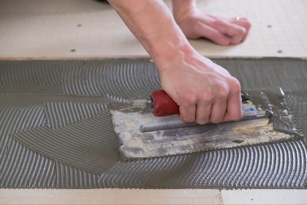 Tile setter using a trowel to spread tile adhesive