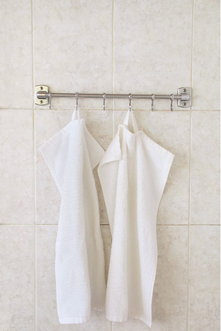 Two white terry towels on a hanger on the background of a wall of ceramic tiles