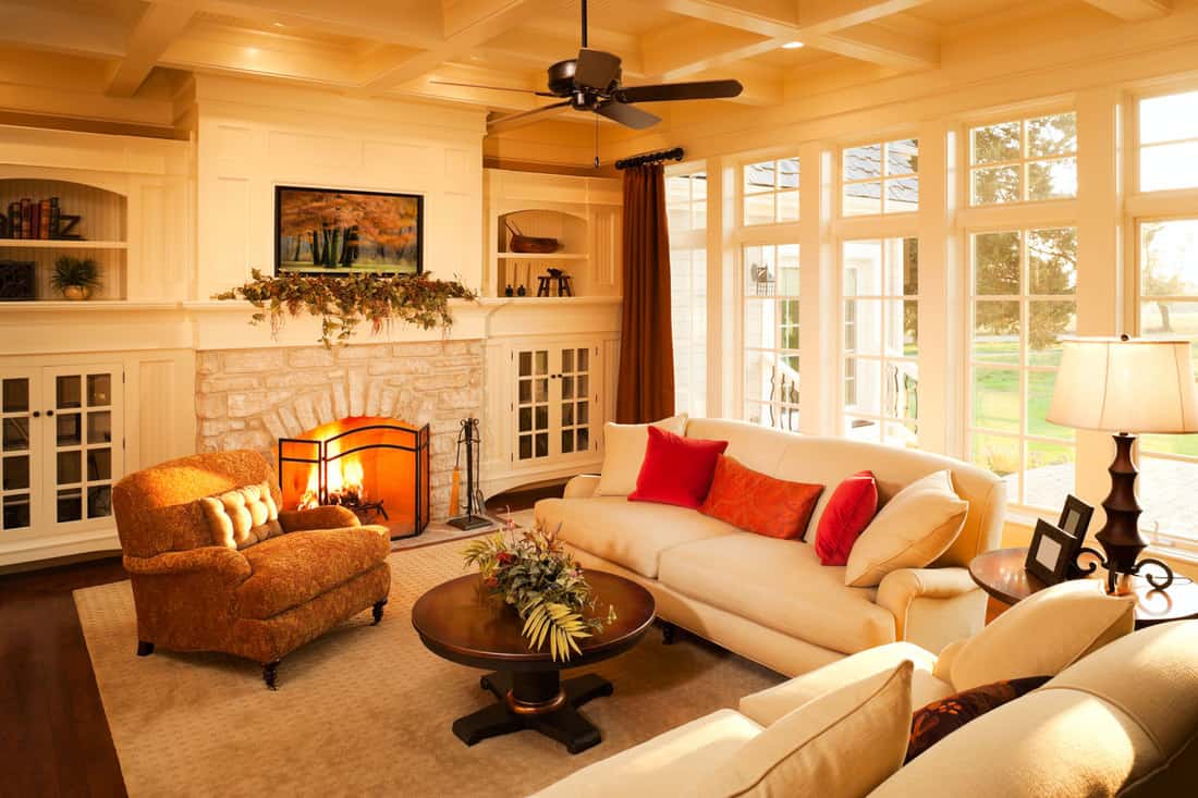 Warm afternoon sunlight pours into an elegant homes living room with a stone fireplace and large windows looking out into the yard with loveseat and sofa, Does A Sofa Have To Match The Loveseat?