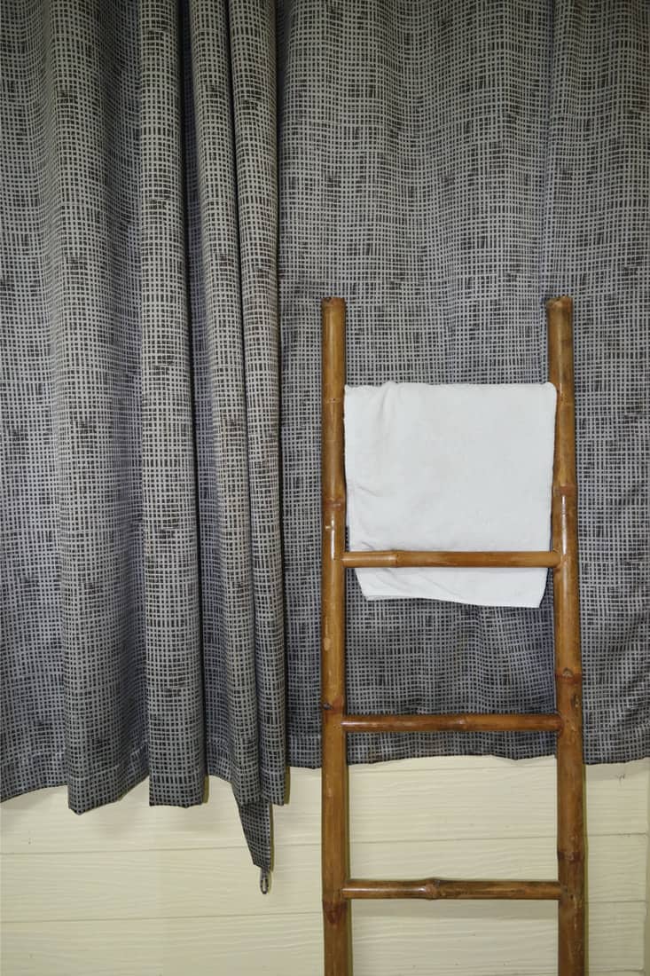 Serviette de couleur blanche à accrocher sur un support en tissu d'échelle en bambou avec un rideau gris en arrière-plan