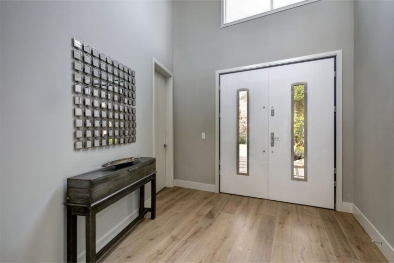 White front door opens to a contemporary two story grey foyer fitted with a black console table positioned under metal mirror wall art. Northwest, USA
