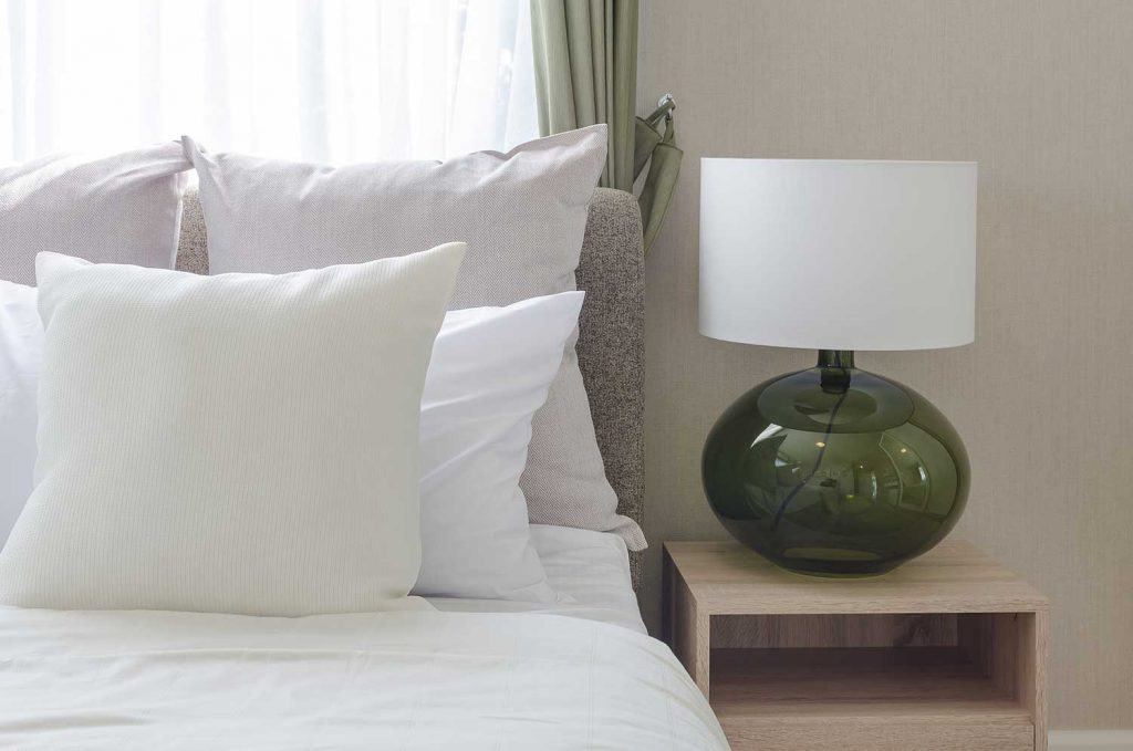 White pillows on bed with modern white lamp on wooden table side