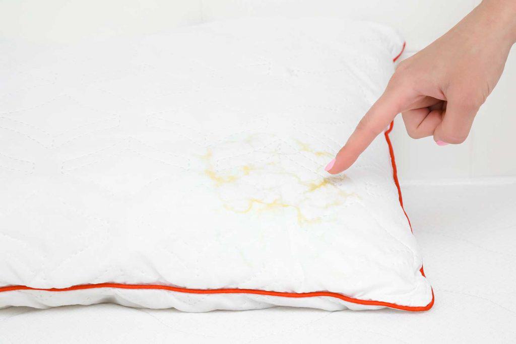 Woman's hand finger pointing to saliva stain on white pillow