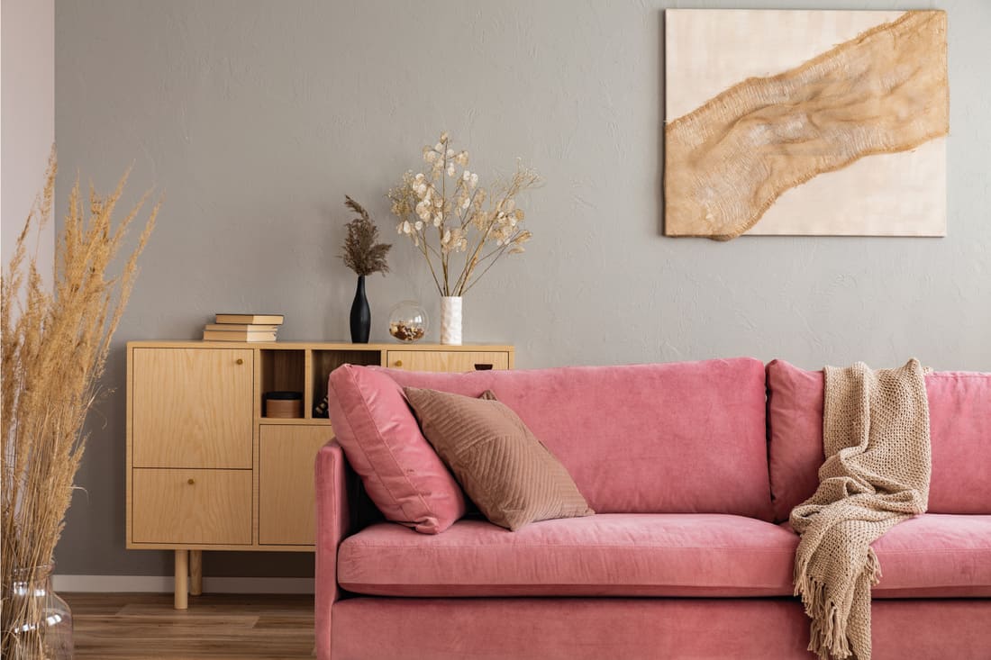 Wooden console table and abstract painting behind pink couch in elegant living room interior