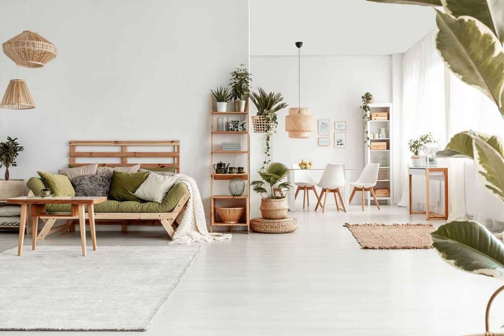 Wooden table in front of green sofa in white spacious flat interior with plants, rug and lamps