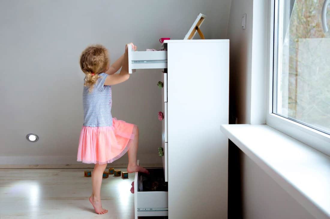 Young girl child climbing on modern high dresser furniture, danger of dresser dipping over concept. Children home hazards.