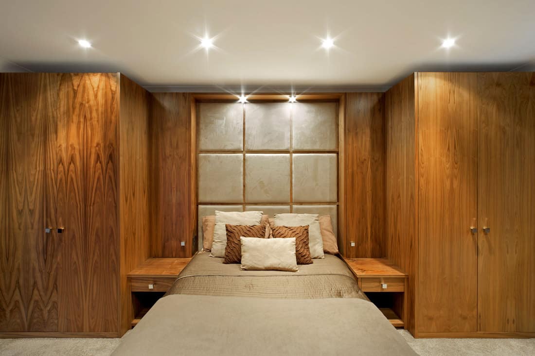 a bedroom generously fitted with beautiful walnut panelling, wardrobes, bedside tables, cupboards and headboard 