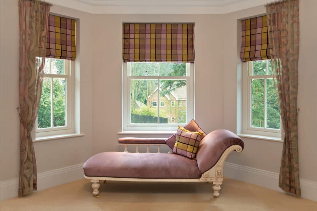 a traditional pink chaise longue in the bay window of a girl's bedroom in a luxury new home
