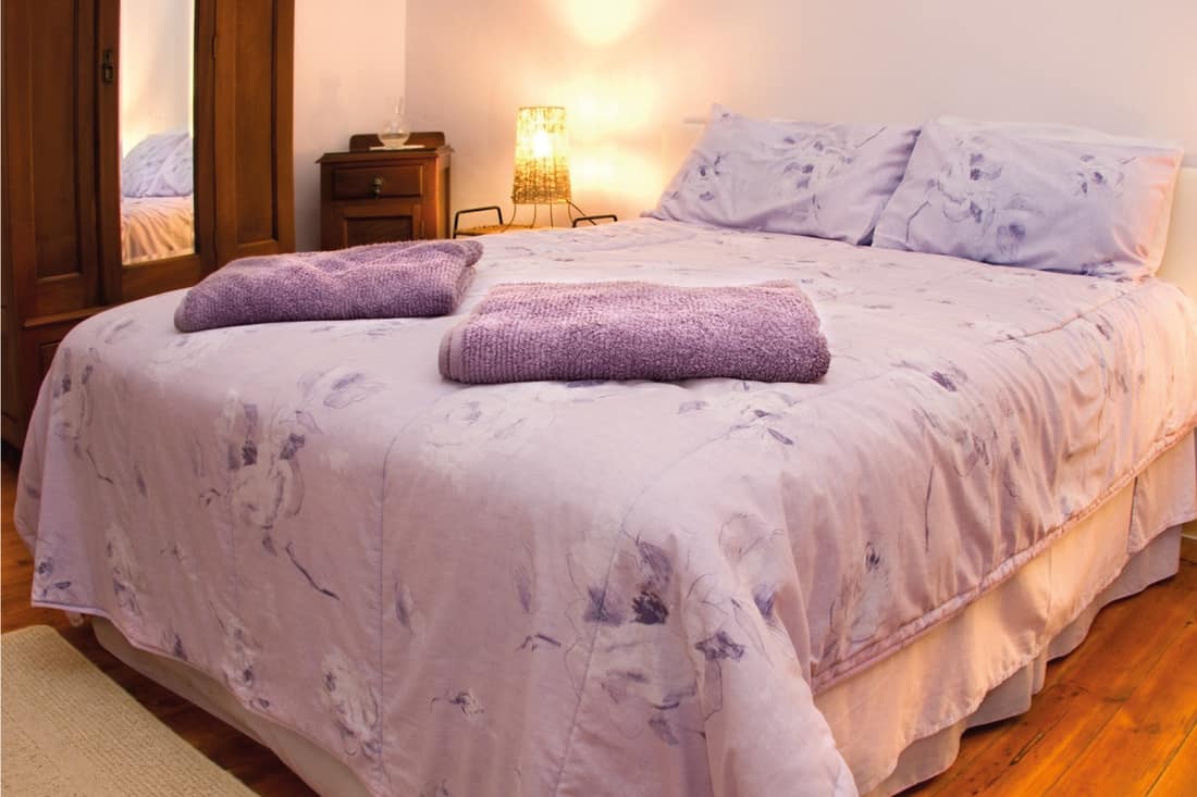 Country bedroom in rustic style, light purple beddings and towels