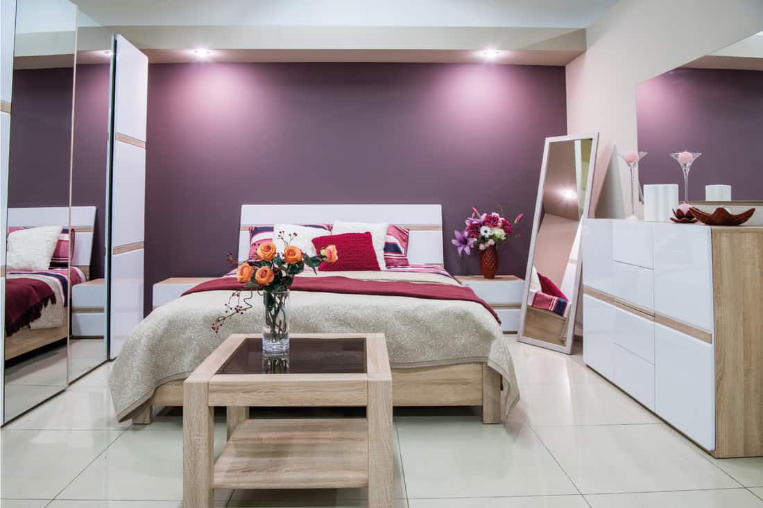 Cozy modern bedroom interior in purple tones, mirrors on the sides of the bed and flower in the vase on a small table