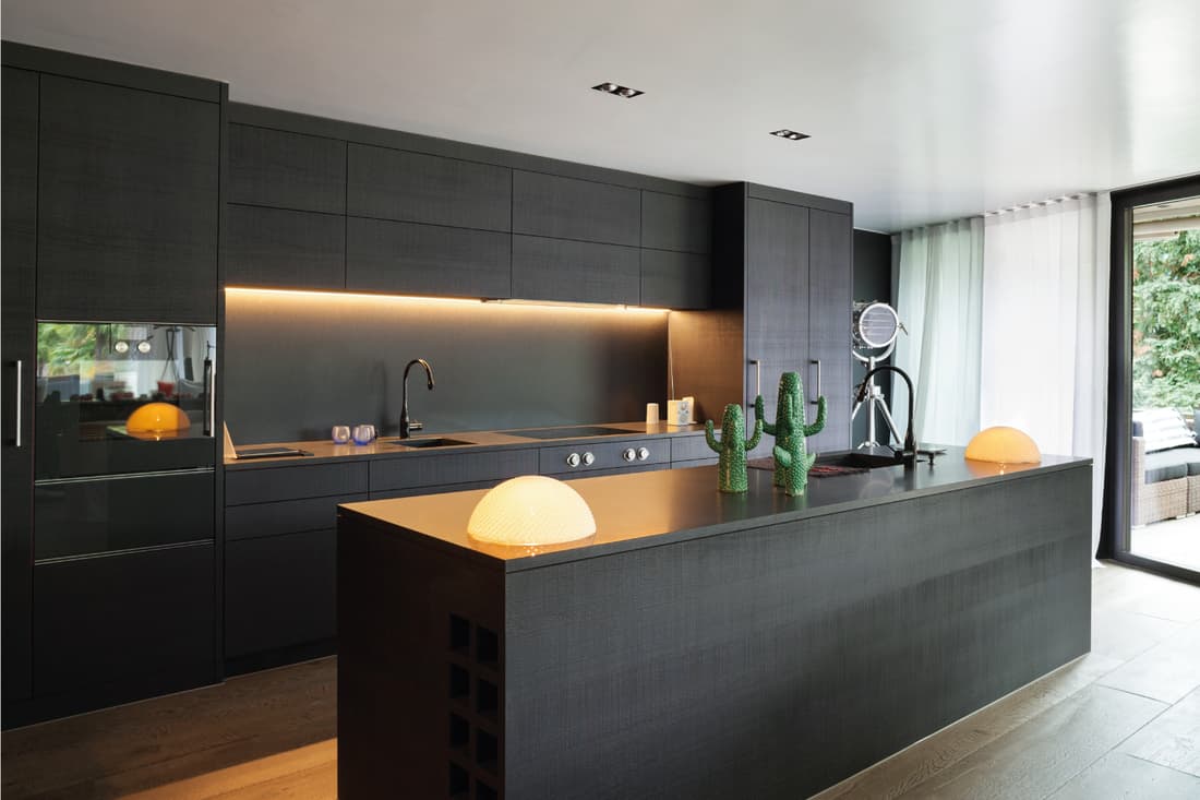 Kitchen with black furniture and wooden floor, kitchen island, lights under the cabinet on top of the sink