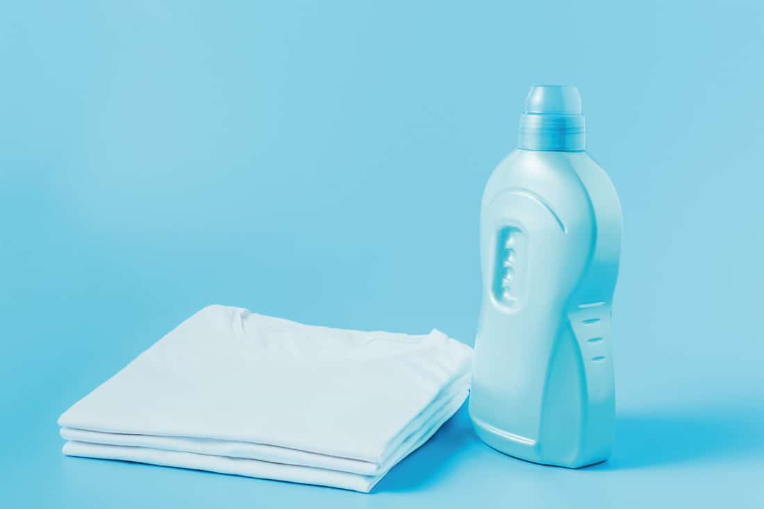Laundry liquid and stack of white clean t-shirts on blue background