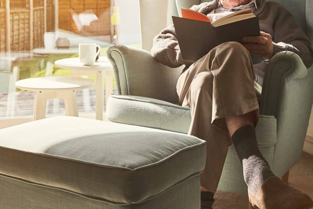 Mature man sitting on arm chair and reading a book at home