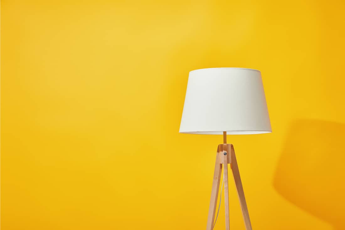Tripod floor lamp with white shade in front of a bright yellow wall, What Type Of Floor Lamp Gives The Most Light?