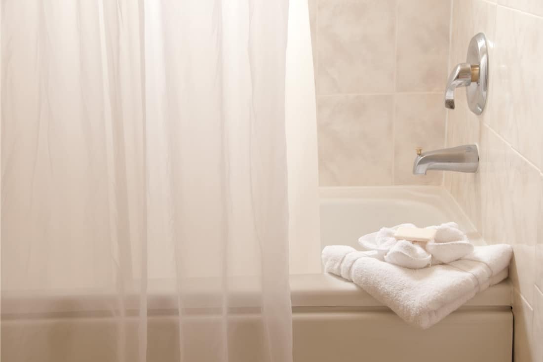 Tub with towels in a white bathroom, How To Hang A Shower Curtain [Even Without Hooks]