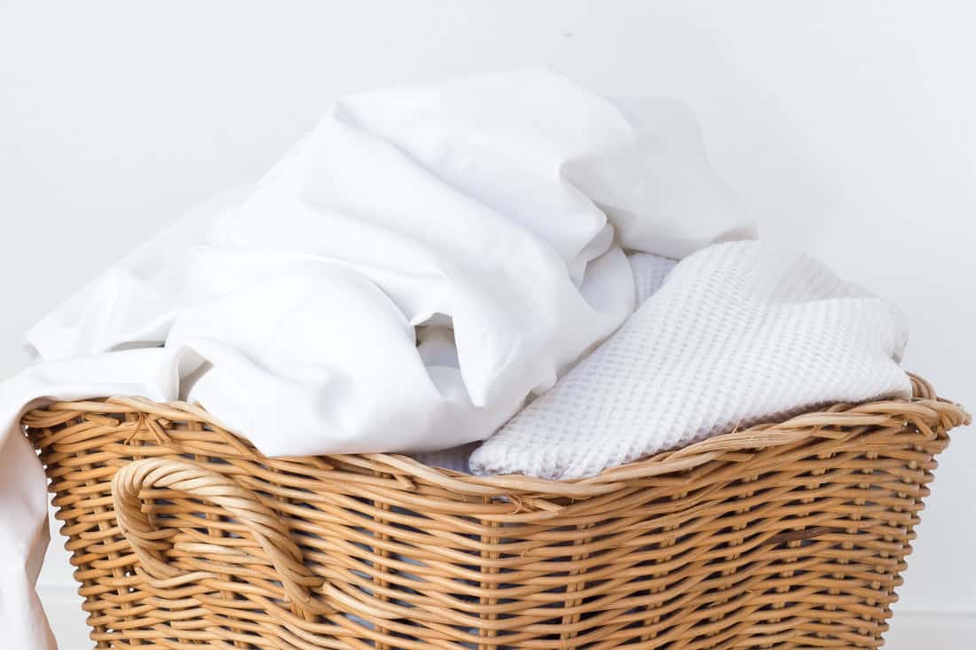 wicker laundry basket filled with dirty laundry white bedding, How To Wash White Bedding (With And Without Bleach)