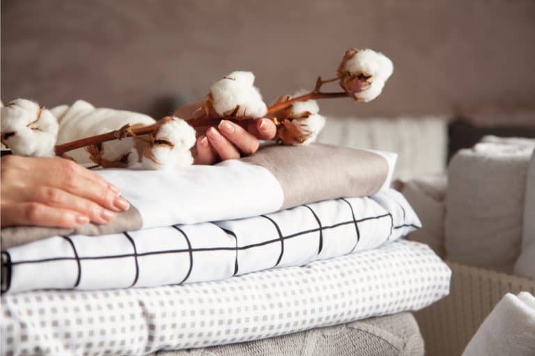 woman hands holding the cotton branch with pile of neatly folded bed sheets, blankets and towels, How To Bleach White Sheets And Towels