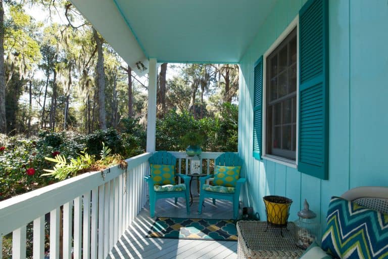 A blue colored porch with blue wooden chairs, blue throw pillows, and a white colored fence, Do Blue Ceilings Keep Bugs Away?