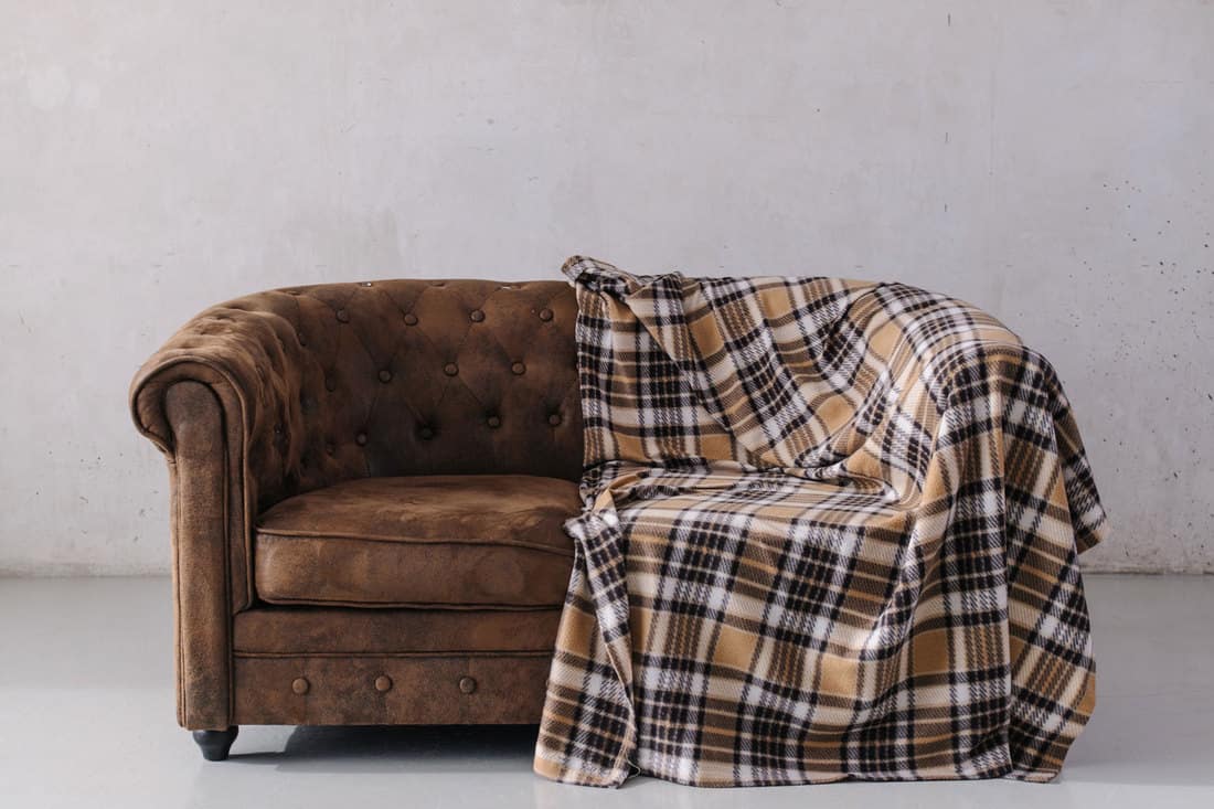 A brown sofa with a brown checkered blanket on it inside a gray living room