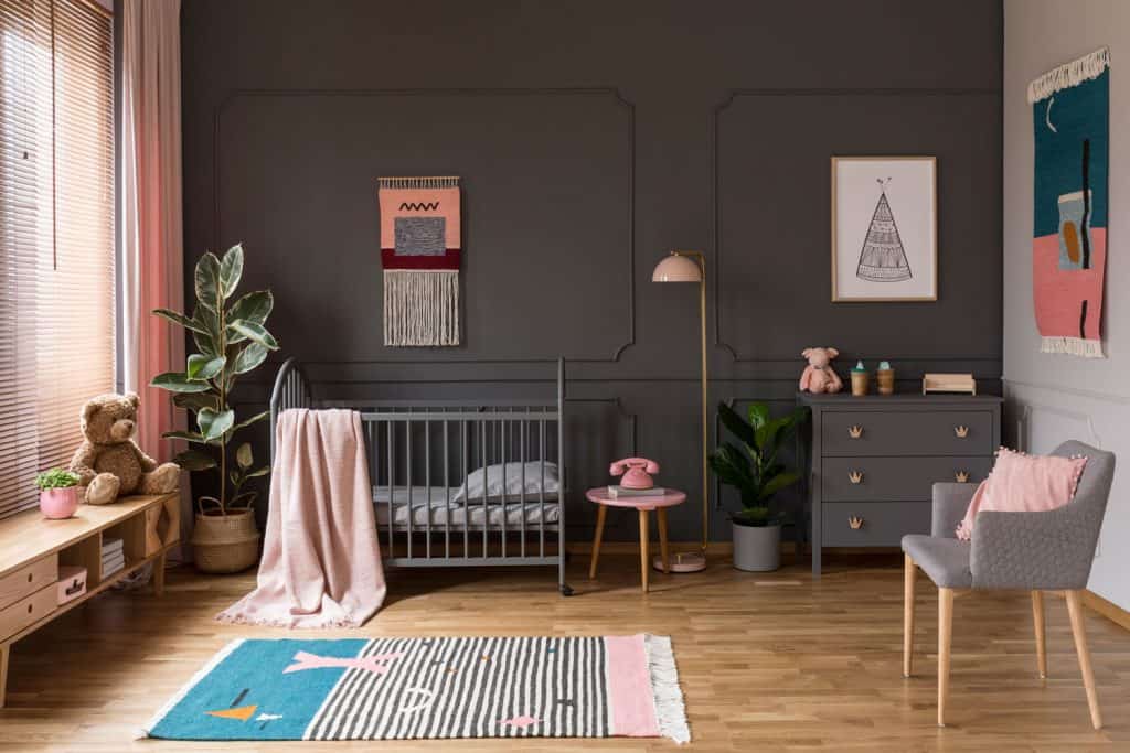 A Childs room with a gray wall, gray crib and cabinets, and wooden laminated flooring