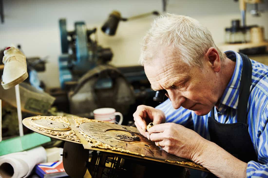 A clock maker using an eye loupe, working on an antique clock.