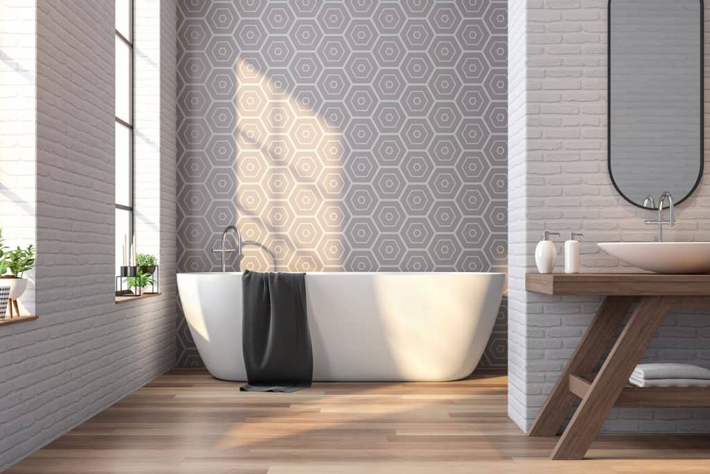 A contemporary bathroom with gray hexagonal patterned wall, a white bathtub, and indoor plants placed on the window