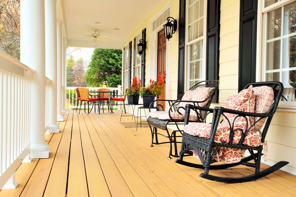 A country themed front porch with black rocking chairs and shutters and decorative plants outside